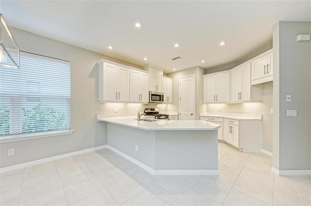 A kitchen features white cabinets, light countertops, a peninsula, and tile flooring — 5564 SUMMIT GLEN, BRADENTON, FL