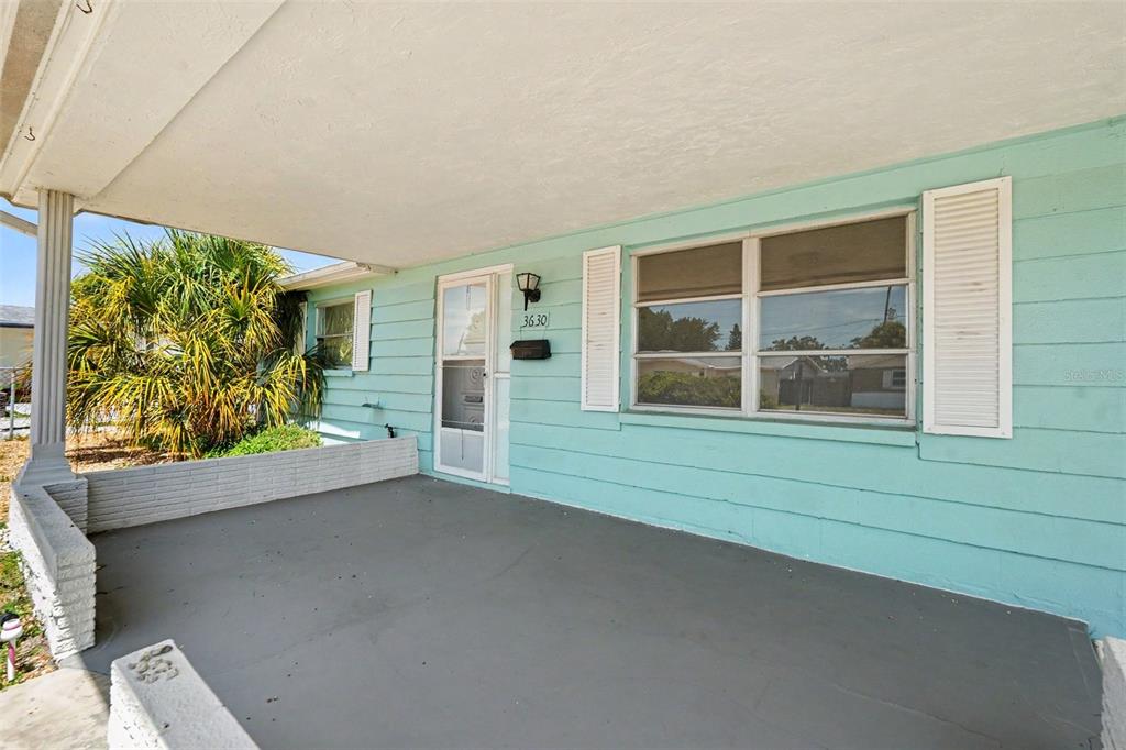 A covered concrete porch features light blue siding, white shutters, and a glass storm door — 3630 WINDER DR, HOLIDAY, FL
