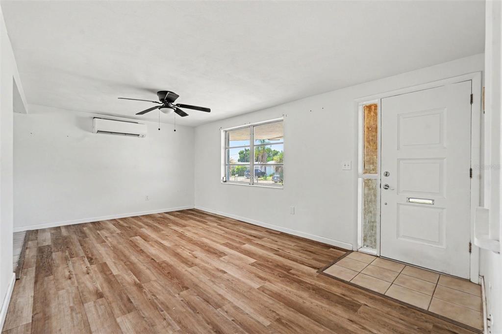 An empty living room features wood-look flooring, a ceiling fan, and a white front door — 3630 WINDER DR, HOLIDAY, FL