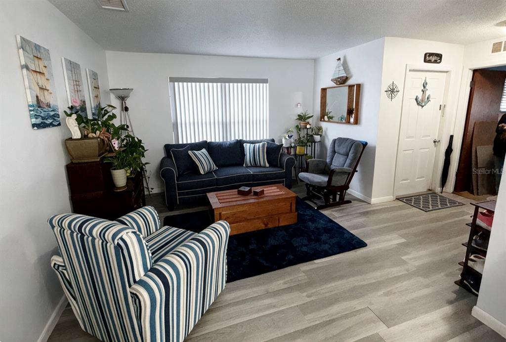 A living room features a blue striped armchair, a dark sofa, and light wood-look flooring — 2846 LANCASTER ROAD, MELBOURNE, FL