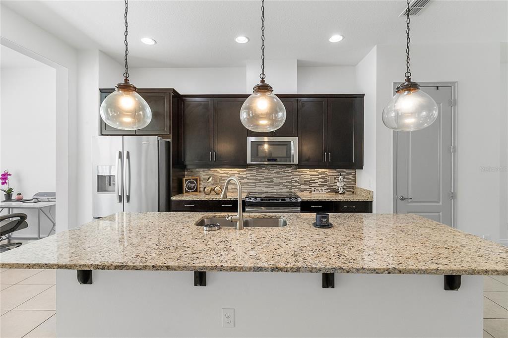 A kitchen features a granite-topped island with a sink, dark cabinets, and three glass pendant lights — 940 LOBELIA DRIVE, LAKE MARY, FL