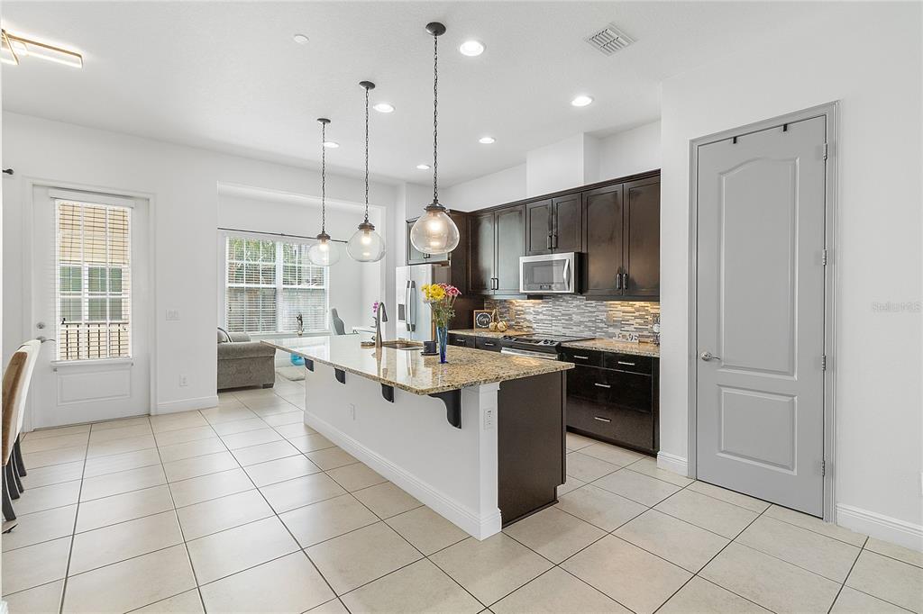 A kitchen features dark wood cabinets, granite countertops, a central island, and light tile flooring — 940 LOBELIA DRIVE, LAKE MARY, FL