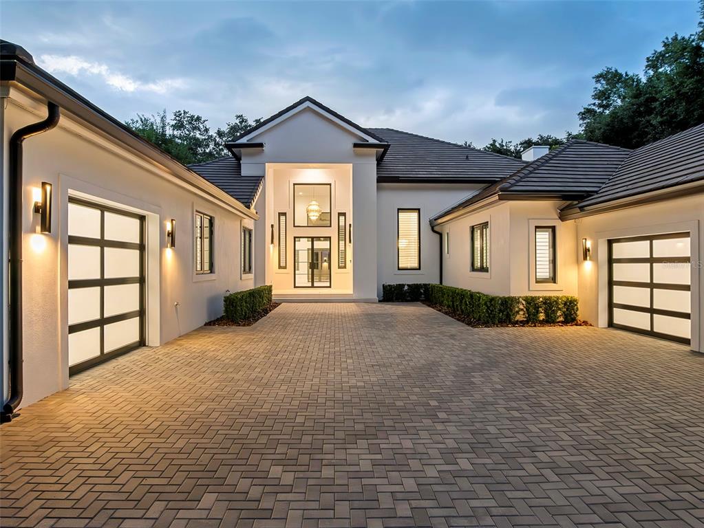 A modern house exterior features a paved courtyard, two glass-paneled garage doors, and a central entrance — 5199 LATROBE DR, WINDERMERE, FL