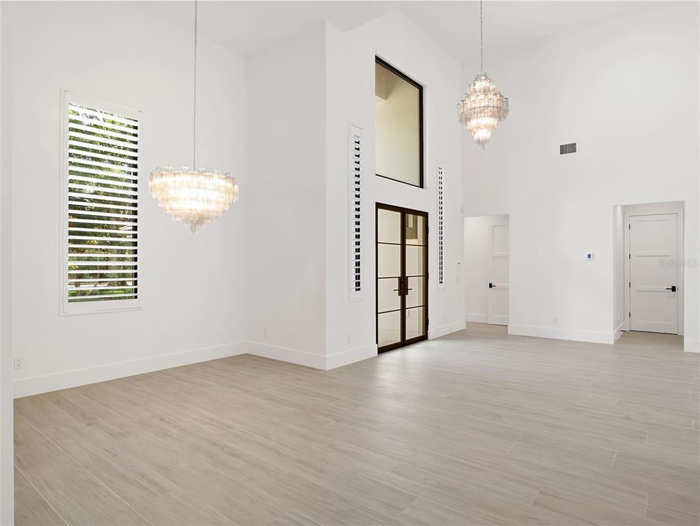 A bright, high-ceilinged room features light wood-look tile floors, two crystal chandeliers, and glass doors — 5199 LATROBE DR, WINDERMERE, FL