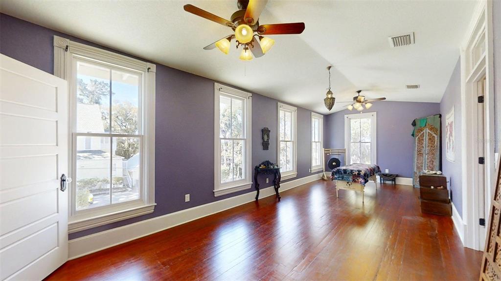 A spacious room with purple walls, hardwood floors, multiple windows, and two ceiling fans — 805 E FORT KING STREET, OCALA, FL