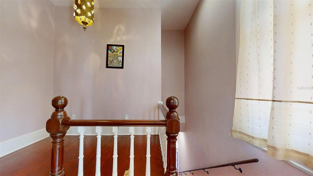 A wooden staircase railing overlooks a landing with light pink walls and hardwood floors — 805 E FORT KING STREET, OCALA, FL