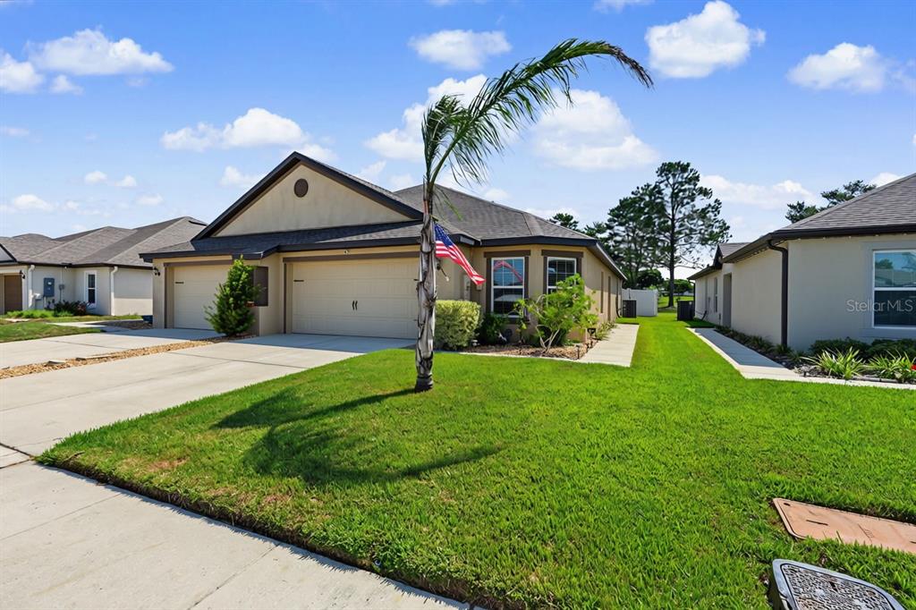 A tan single-story house with a two-car garage and a palm tree in the front yard — 8951 SOUTHERN CHARM CIRCLE, BROOKSVILLE, FL