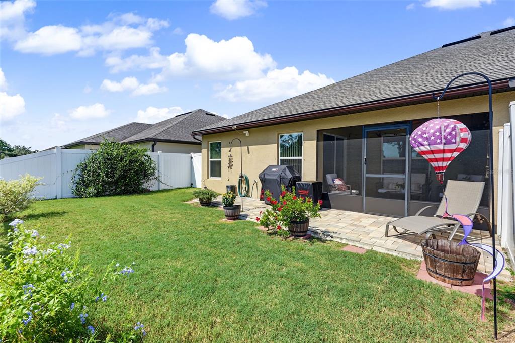 A backyard features a paved patio, a screened-in porch, a grill, and a white fence — 8951 SOUTHERN CHARM CIRCLE, BROOKSVILLE, FL