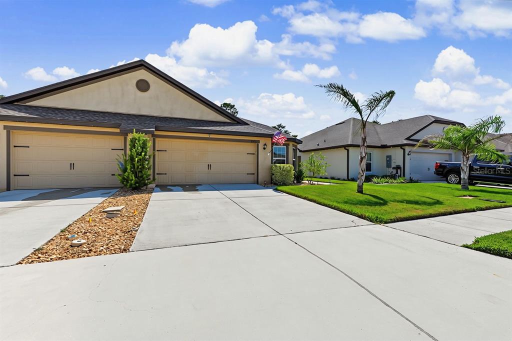 A tan duplex house with two garage doors and a concrete driveway under a blue sky — 8951 SOUTHERN CHARM CIRCLE, BROOKSVILLE, FL