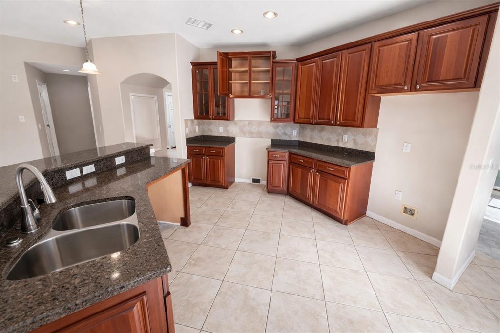 A kitchen features cherry wood cabinets, granite countertops, tile flooring, and a double-basin sink — 3734 MOON DANCER PLACE, ST CLOUD, FL