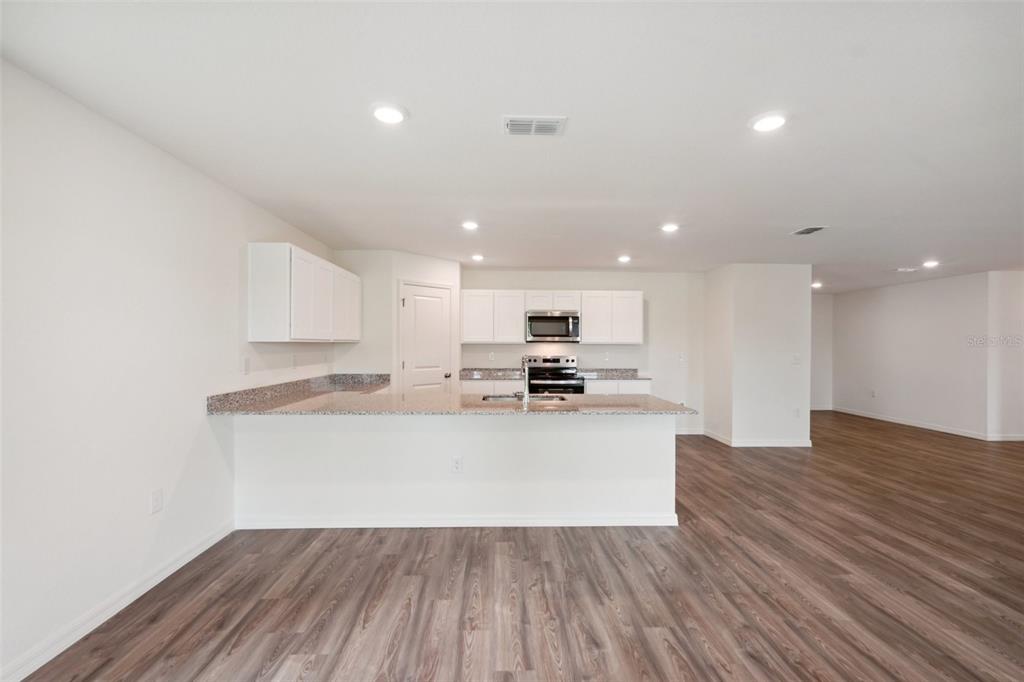 A kitchen with white cabinets, granite countertops, and wood-look flooring opens to a living area — 12038 PEMBROOKE AVENUE, WEEKI WACHEE, FL