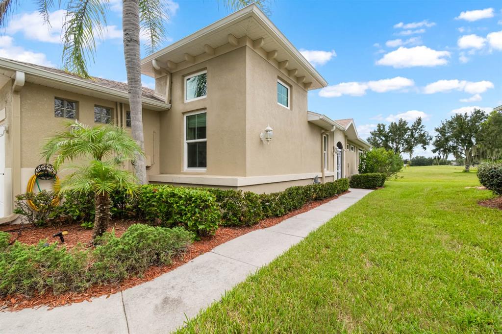 A beige stucco house exterior features a concrete walkway, landscaping, and a grassy yard — 1160 JAMESON GREENS DRIVE, SUN CITY CENTER, FL