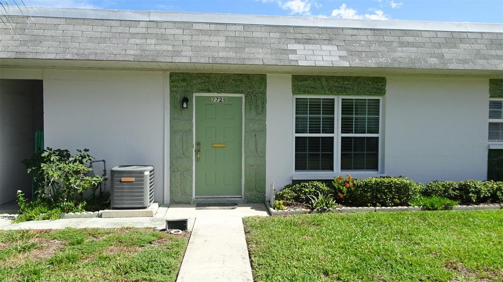 A single-story residential unit features a green front door, white siding, and a gray roof — 7729 39TH TERRACE N, ST PETERSBURG, FL