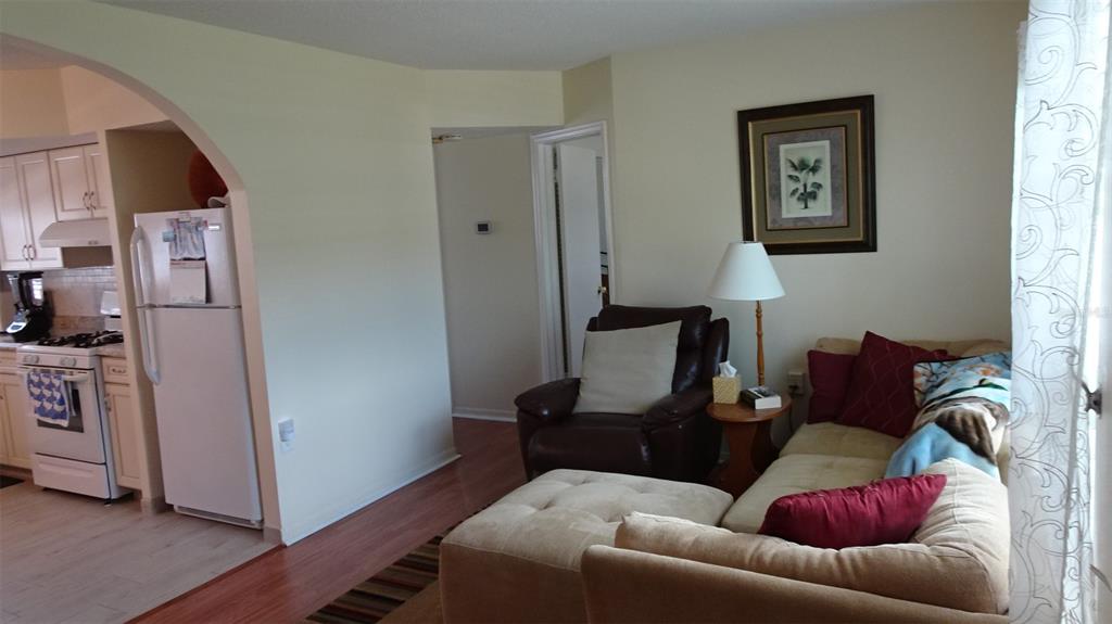 A living room with a sectional sofa and recliner opens into a kitchen with white appliances — 7729 39TH TERRACE N, ST PETERSBURG, FL