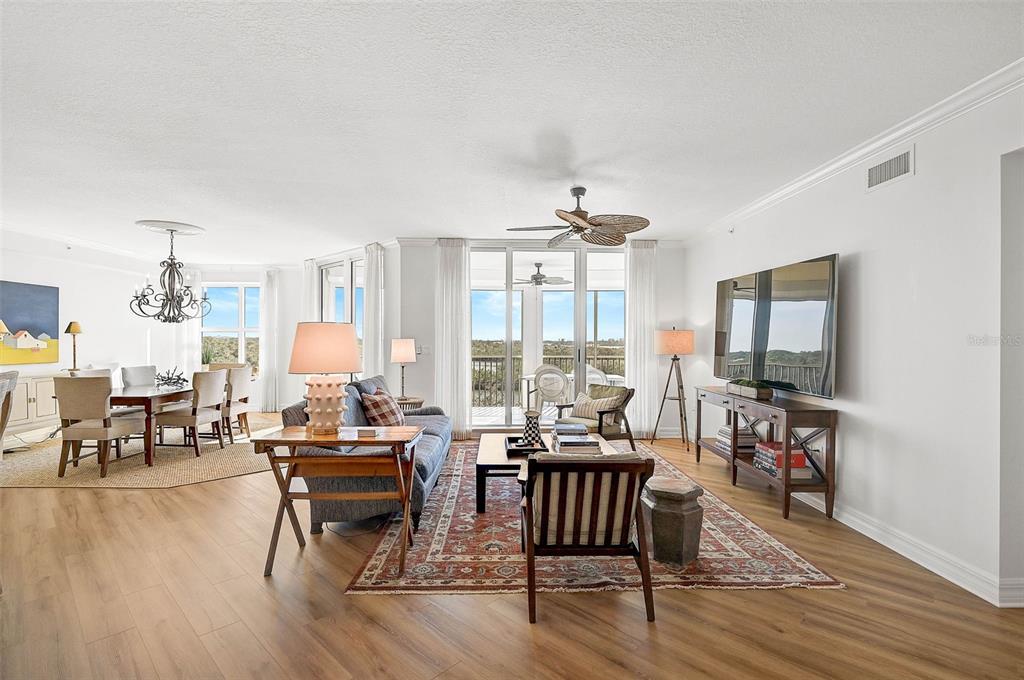 A bright living and dining area features wood-look flooring, a ceiling fan, and balcony access — 3603 N POINT ROAD UNIT 602, OSPREY, FL