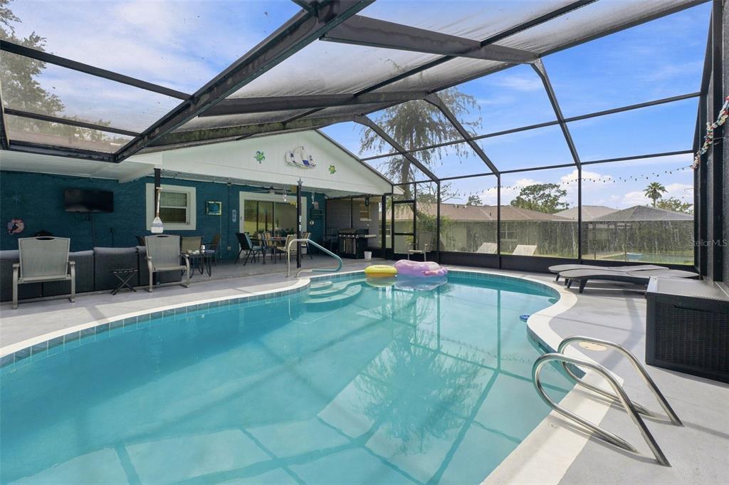 A screened-in patio features a swimming pool, lounge chairs, and a covered outdoor living area — 12411 BROOKSIDE STREET, SPRING HILL, FL