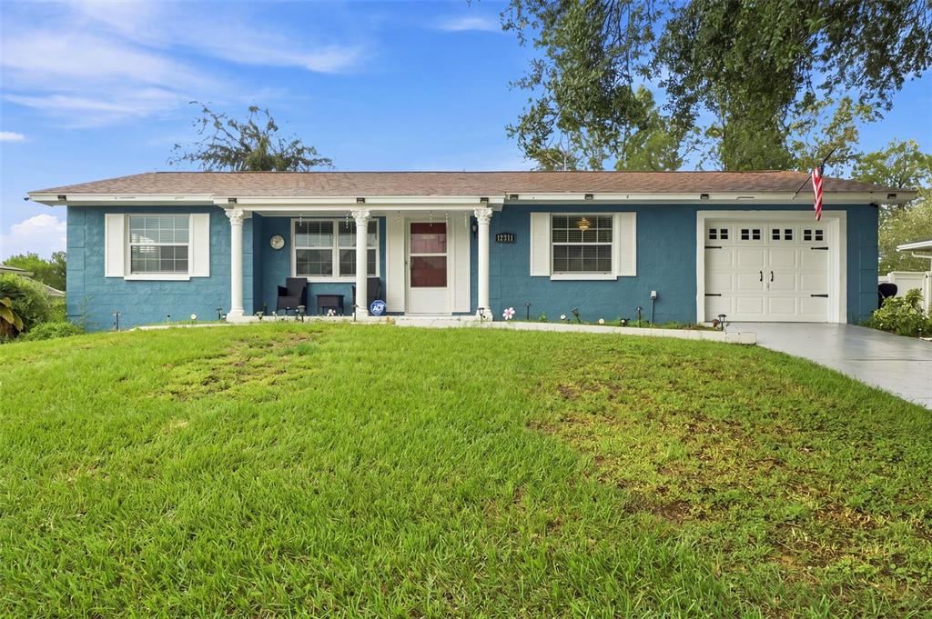A blue, single-story ranch-style house features a white front door, columns, and an attached garage — 12411 BROOKSIDE STREET, SPRING HILL, FL