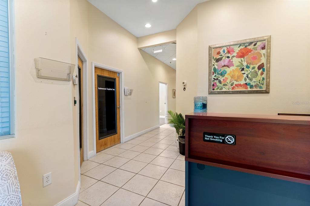An office reception area features a wooden desk, tiled floors, and a floral wall painting — 8810 COMMODITY CIR UNIT 36, ORLANDO, FL