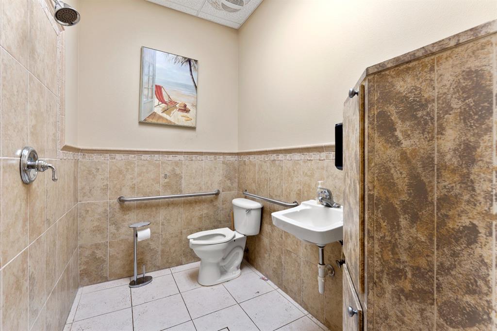 A tiled bathroom features a toilet, a wall-mounted sink, grab bars, and a shower head — 8810 COMMODITY CIR UNIT 36, ORLANDO, FL