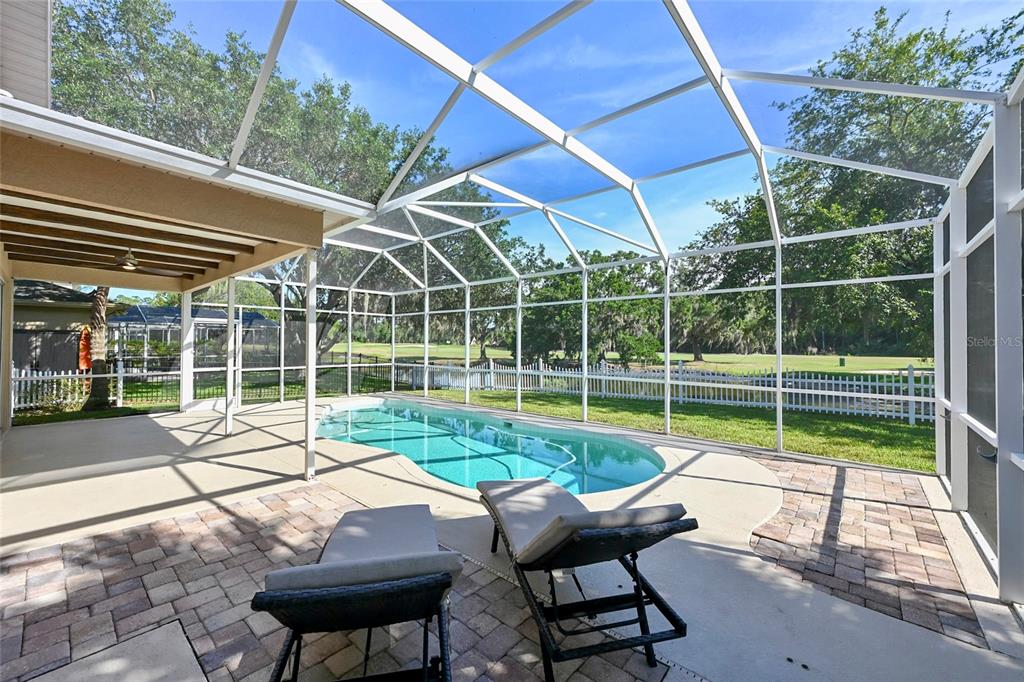A screened-in patio features a swimming pool, lounge chairs, and a view of a golf course — 4906 AUGUSTA AVENUE, OLDSMAR, FL