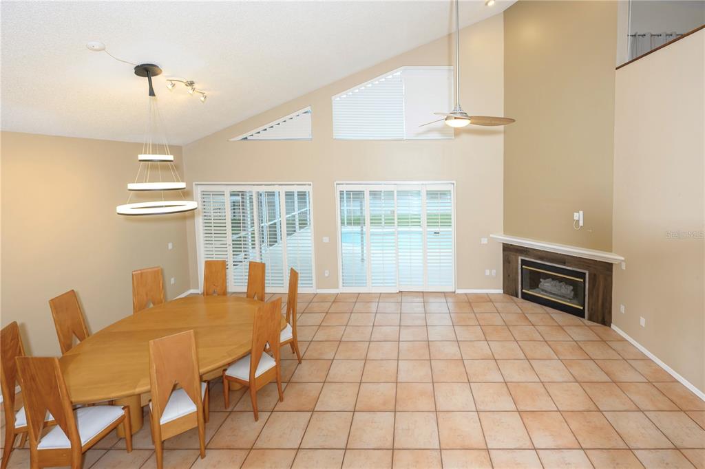 A dining area with tile floors, a wooden table, and a fireplace under vaulted ceilings — 4906 AUGUSTA AVENUE, OLDSMAR, FL