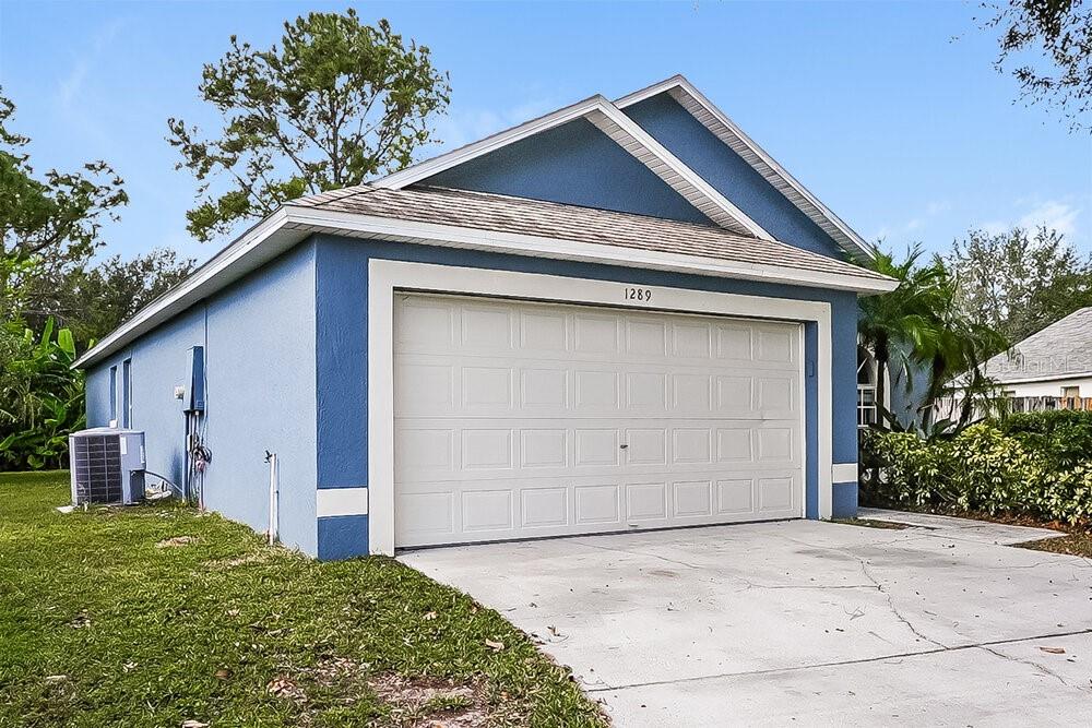 A blue house exterior features a two-car garage, a concrete driveway, and an air conditioning unit — 1289 HIMALAYAN COURT, APOPKA, FL