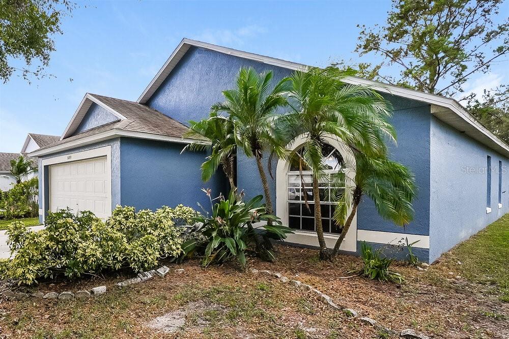 A blue single-story house features a two-car garage, a large arched window, and palm trees — 1289 HIMALAYAN COURT, APOPKA, FL