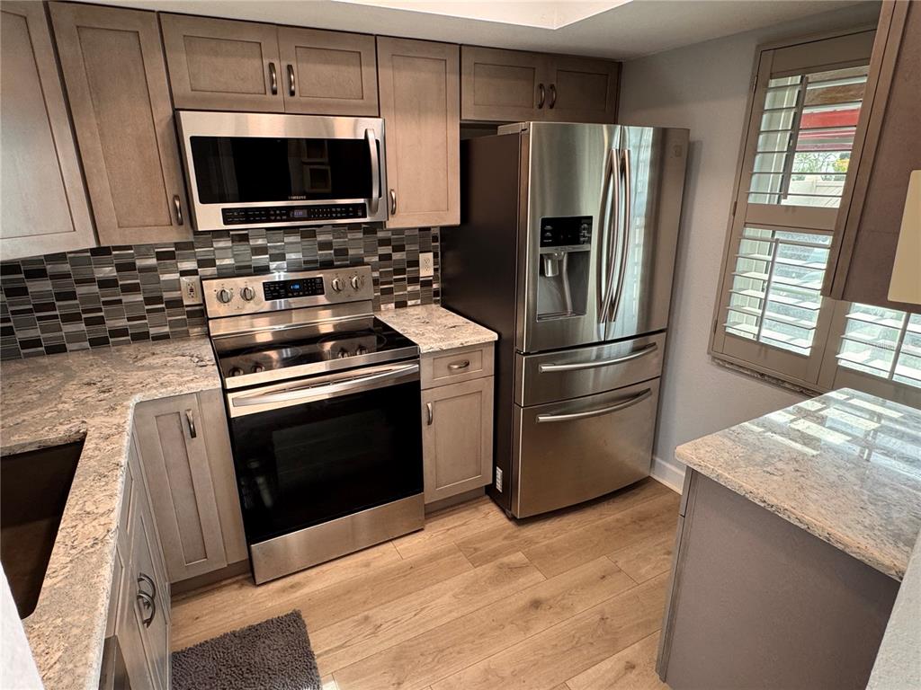 A kitchen features stainless steel appliances, light wood cabinets, granite countertops, and a tiled backsplash — 601 N HERCULES AVENUE UNIT 1404, CLEARWATER, FL