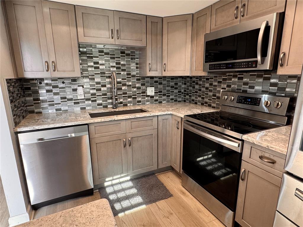 A kitchen features light wood cabinets, stainless steel appliances, and a mosaic tile backsplash — 601 N HERCULES AVENUE UNIT 1404, CLEARWATER, FL