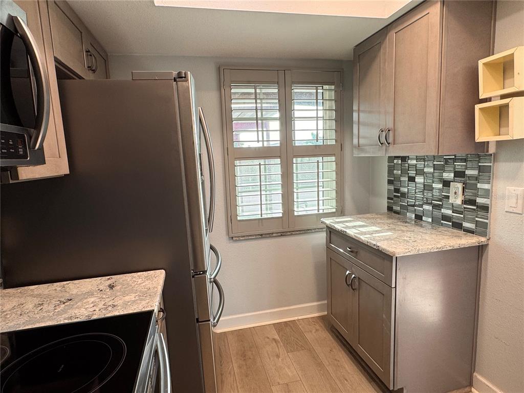 A kitchen features grey cabinets, granite countertops, a mosaic tile backsplash, and stainless steel appliances — 601 N HERCULES AVENUE UNIT 1404, CLEARWATER, FL