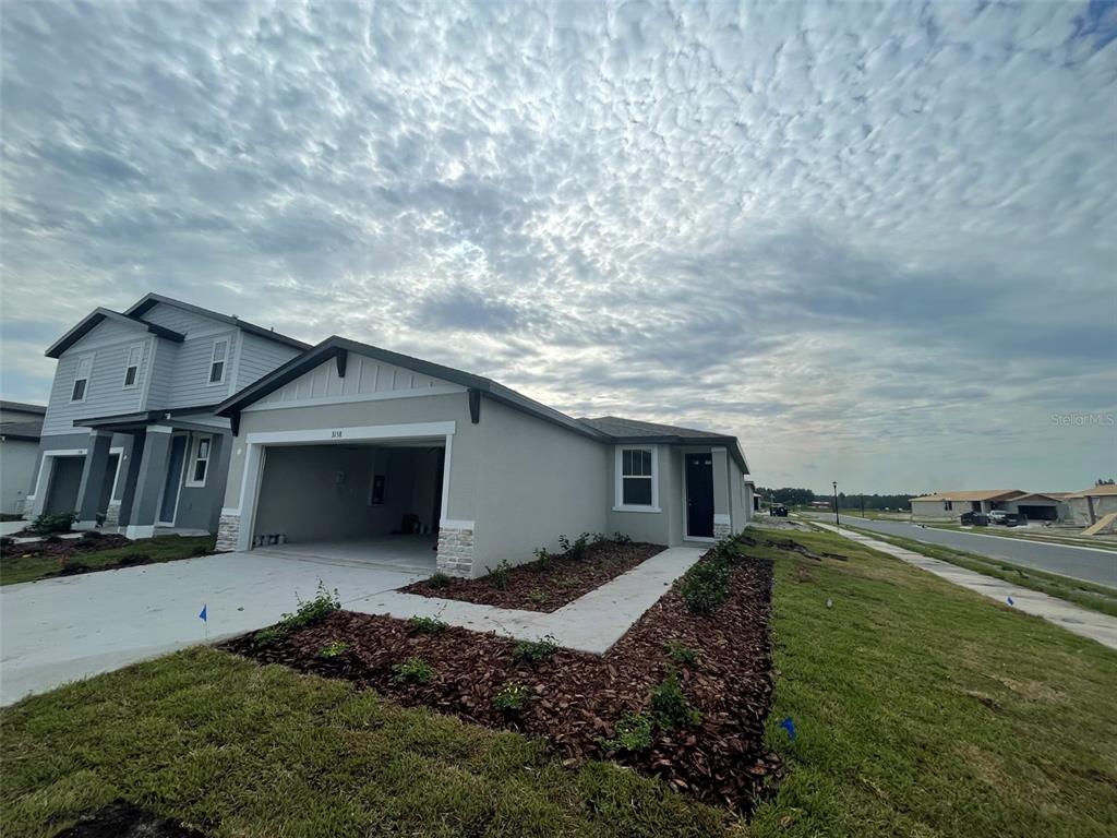 A single-story house with a two-car garage and a concrete walkway under a cloudy sky — 3158 FRESNO PLACE, WESLEY CHAPEL, FL