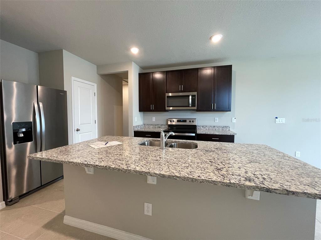 A kitchen features a granite-topped island, stainless steel appliances, and dark wood cabinetry — 3158 FRESNO PLACE, WESLEY CHAPEL, FL