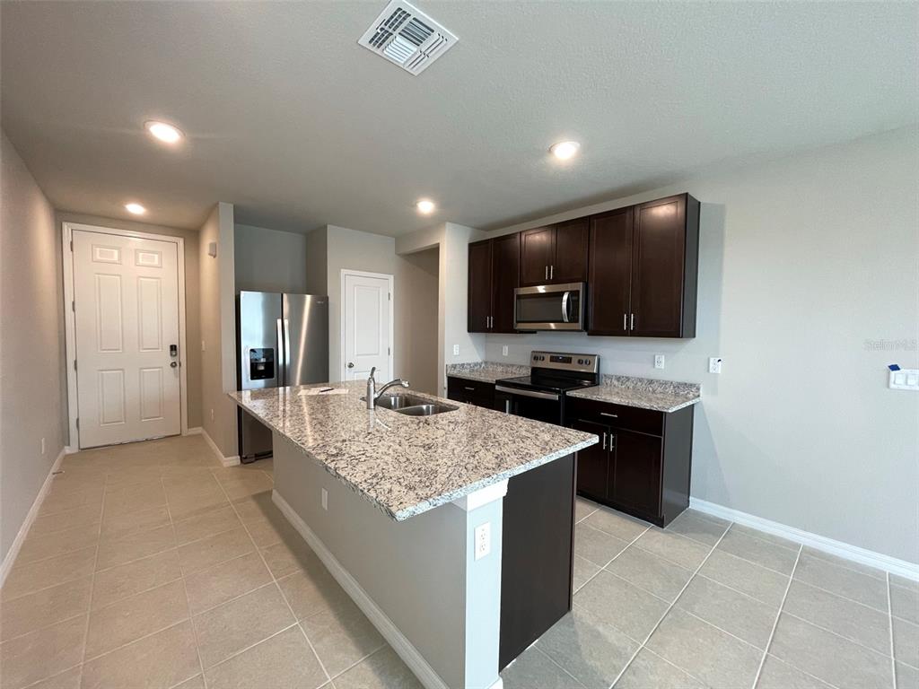 A kitchen features dark wood cabinets, granite countertops, a center island, and stainless steel appliances — 3158 FRESNO PLACE, WESLEY CHAPEL, FL
