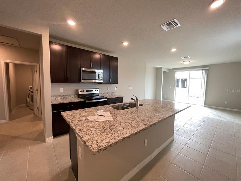 A kitchen features dark wood cabinets, granite countertops, a central island, and tile flooring — 3158 FRESNO PLACE, WESLEY CHAPEL, FL