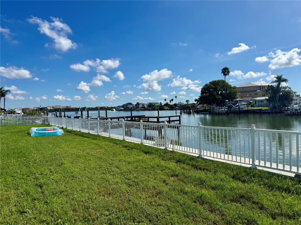 A grassy backyard with a white fence overlooks a canal with boat docks and houses — 722 PRUITT DRIVE, MADEIRA BEACH, FL