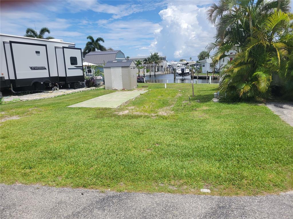 A grassy waterfront lot features a small storage shed and a concrete pad for parking — 138 BAYOU DRIVE, VENICE, FL