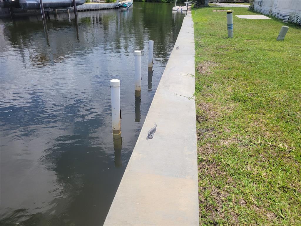 A concrete seawall borders a canal with several white mooring pilings in the water — 138 BAYOU DRIVE, VENICE, FL