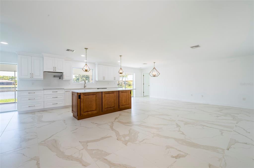 A kitchen with white cabinets, a wood-toned island, and marble-patterned tile flooring — 13797 PINECREST DRIVE, LARGO, FL