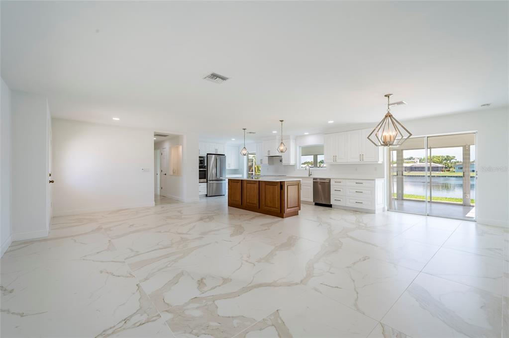 A bright, open-concept kitchen features white cabinetry, a wood-toned island, and large marble-patterned floor tiles — 13797 PINECREST DRIVE, LARGO, FL