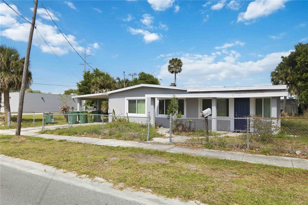 A single-story house with a carport and chain-link fence sits under a blue sky — 214 BLAKE AVENUE, COCOA, FL