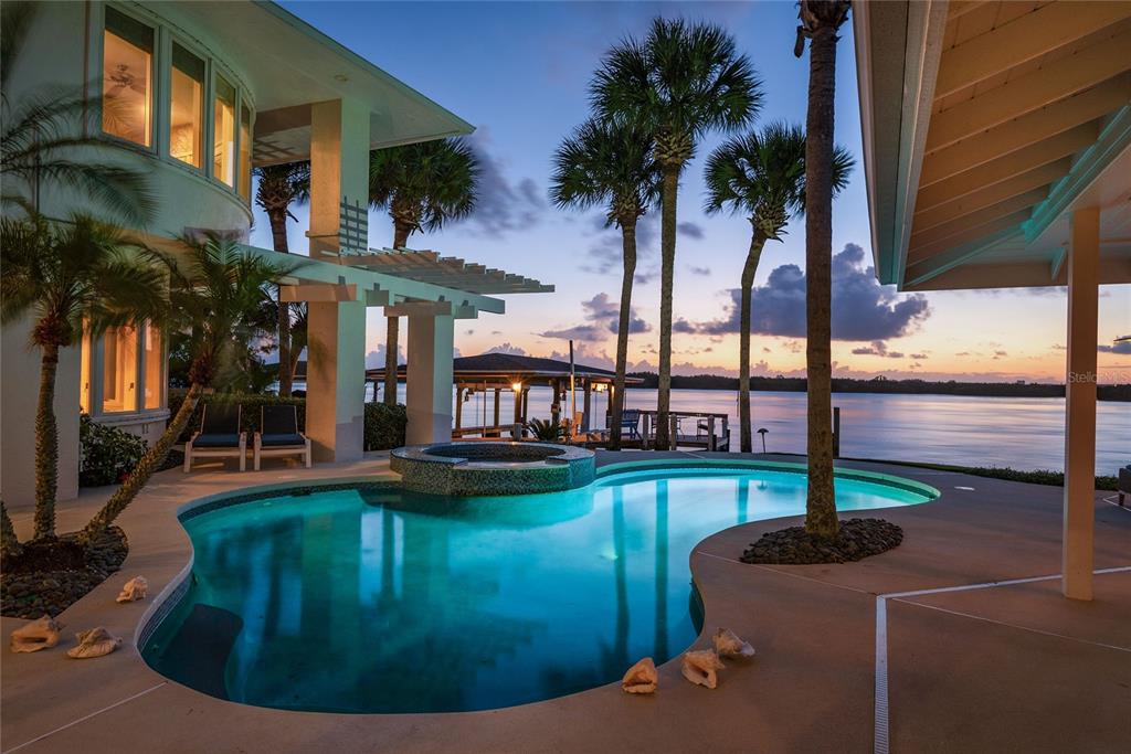 A swimming pool and hot tub sit on a patio overlooking a waterfront sunset view — 1215 COMMODORE DRIVE, NEW SMYRNA BEACH, FL