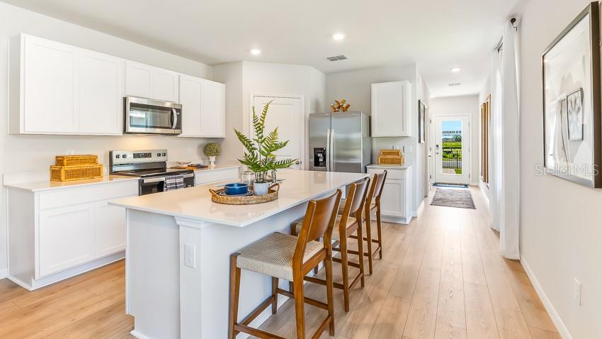 A modern kitchen features white cabinetry, a central island with bar seating, and stainless appliances — 11852 TEXOMA COURT, PARRISH, FL