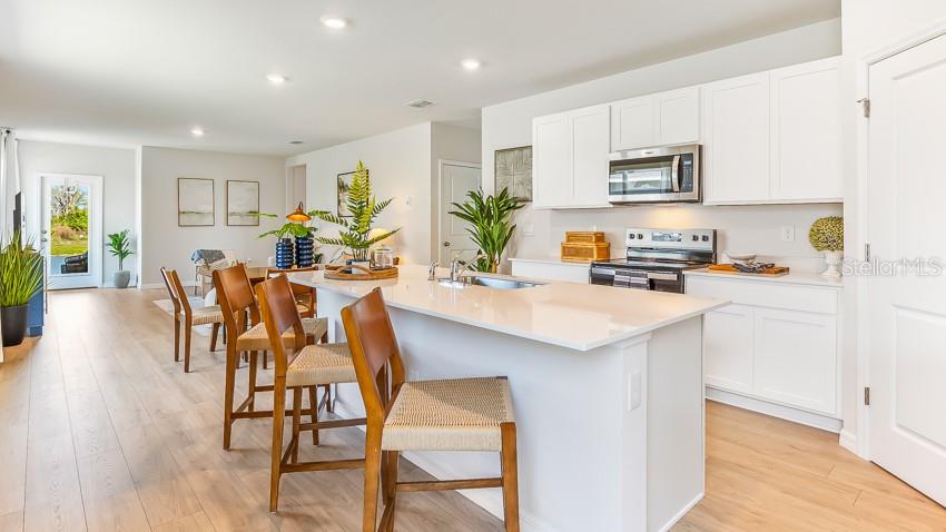 A bright kitchen features white cabinets, a quartz island with bar seating, and light flooring — 11852 TEXOMA COURT, PARRISH, FL