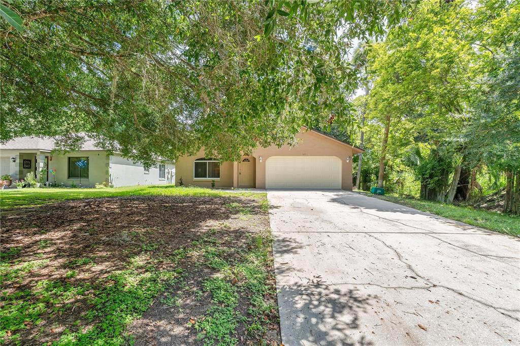 A tan single-story house with a two-car garage and a concrete driveway under large trees — 623 PARQUE DRIVE, ORMOND BEACH, FL