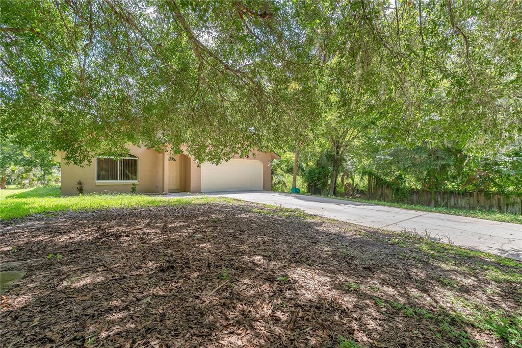 A single-story house with a white garage door sits behind a large tree and driveway — 623 PARQUE DRIVE, ORMOND BEACH, FL