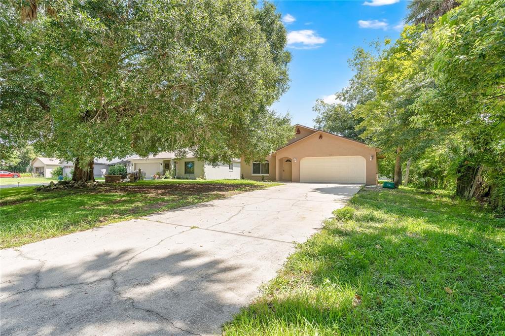 A tan single-story house with a two-car garage and a large tree in the front yard — 623 PARQUE DRIVE, ORMOND BEACH, FL