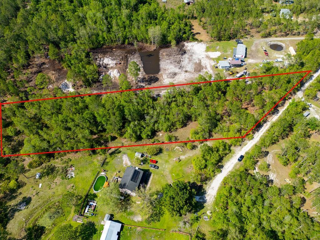 A dirt path runs alongside a dense area of trees and shrubs under a blue sky — 3770 BALSAM COURT, ORMOND BEACH, FL
