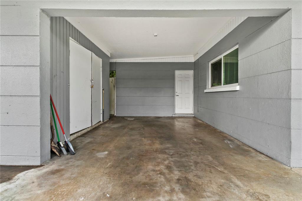A covered concrete carport features gray walls, a white door, and a storage closet — 5711 21ST STREET W, BRADENTON, FL