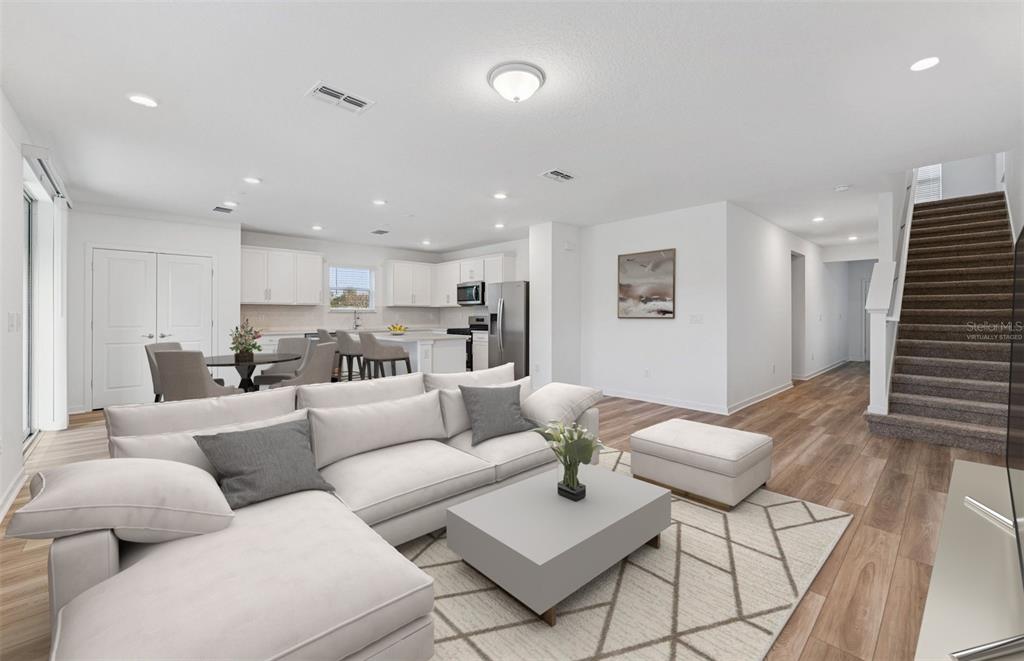 An open-concept living room and kitchen featuring light wood floors, white cabinetry, and a staircase — 9748 CRESCENT MOON DRIVE, RIVERVIEW, FL