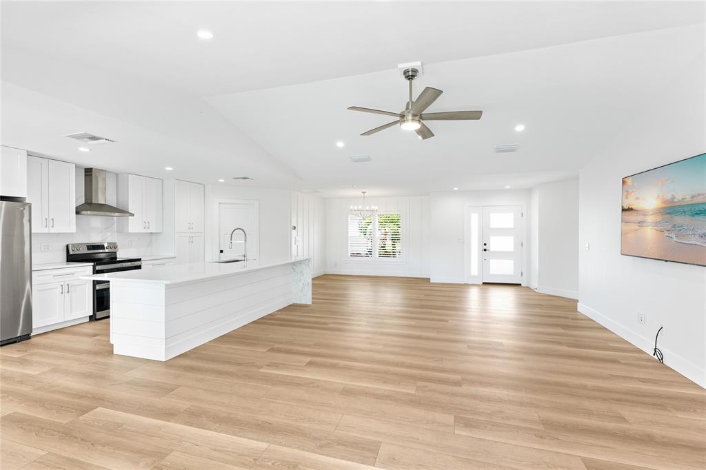 An open-concept living room and kitchen featuring white cabinetry, a stone fireplace, and wood flooring — 206 73RD STREET NW, BRADENTON, FL